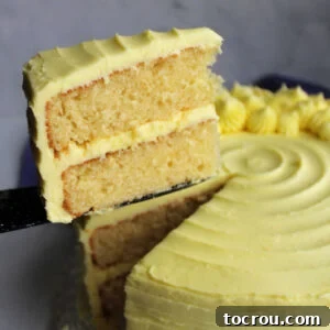Lifting the first slice of lemon velvet cake off the cake plate showing the two layers of pale yellow cake with plenty of yellow lemon buttercream.