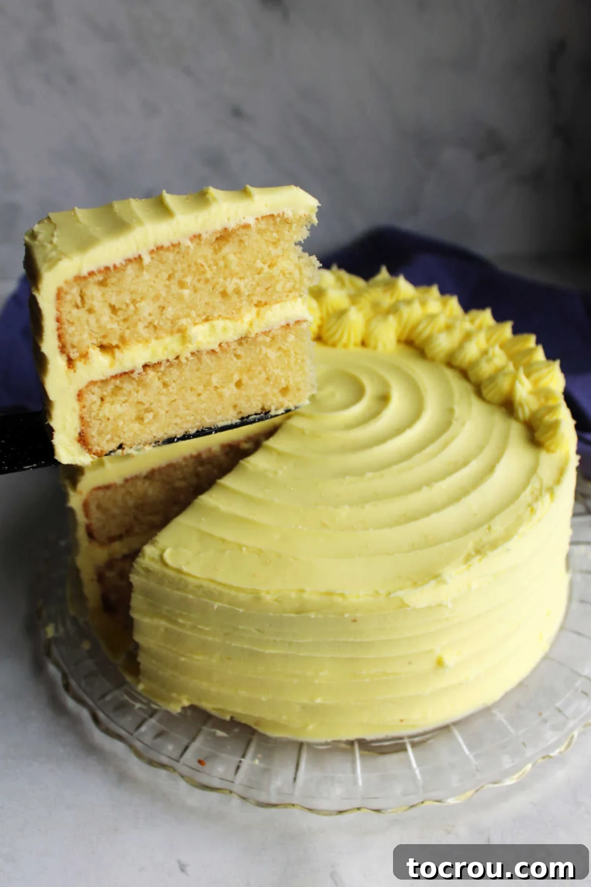 Slice of lemon velvet layer cake with plenty of lemon condensed milk buttercream between the layers and on the outside of the cake.