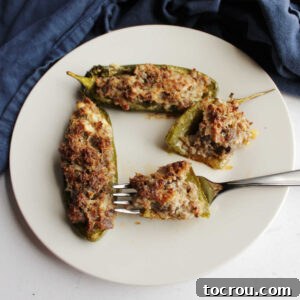 Plate of jalapeno pepper halves stuffed with sausage and cream cheese with a bite on a fork ready to eat.