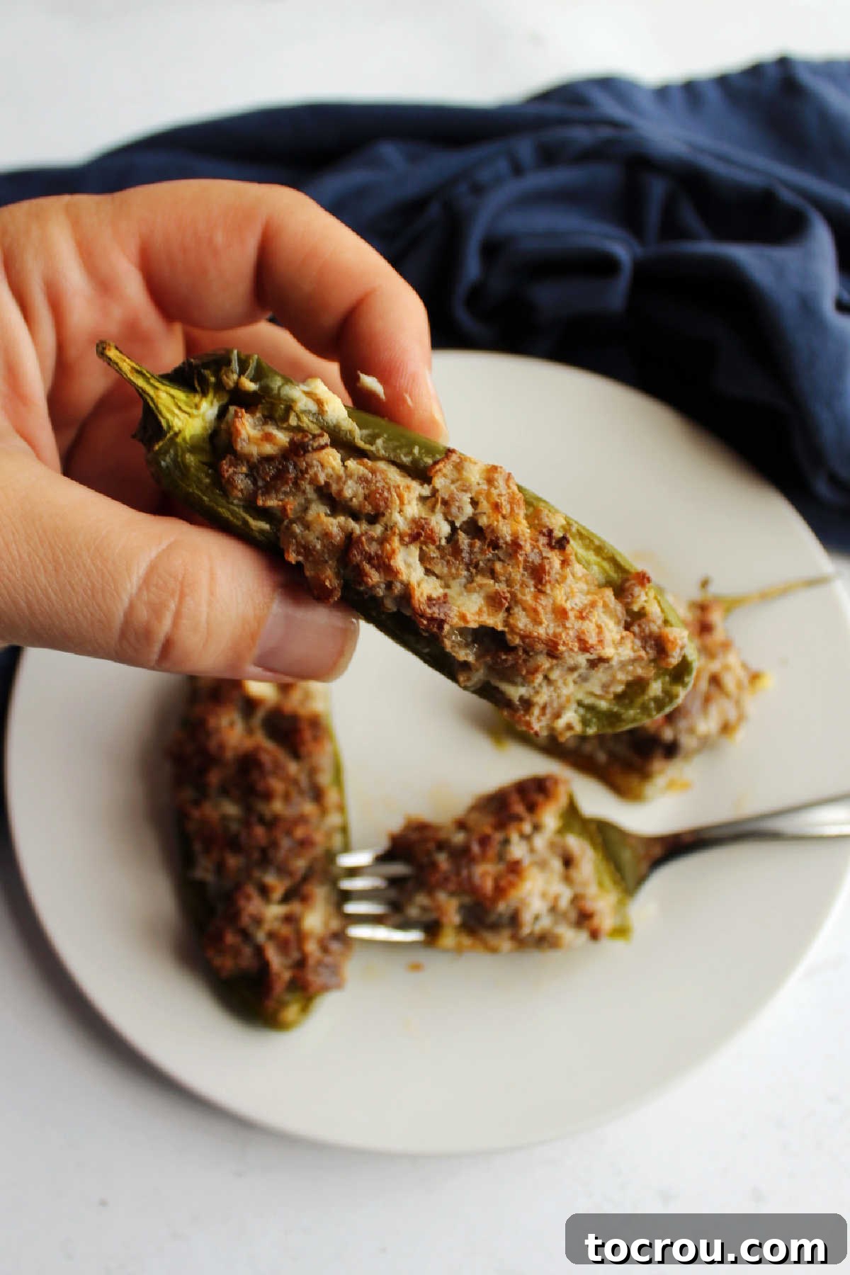 A hand holding a perfectly cooked sausage and cream cheese stuffed jalapeno half, showcasing its golden-brown top and creamy filling.