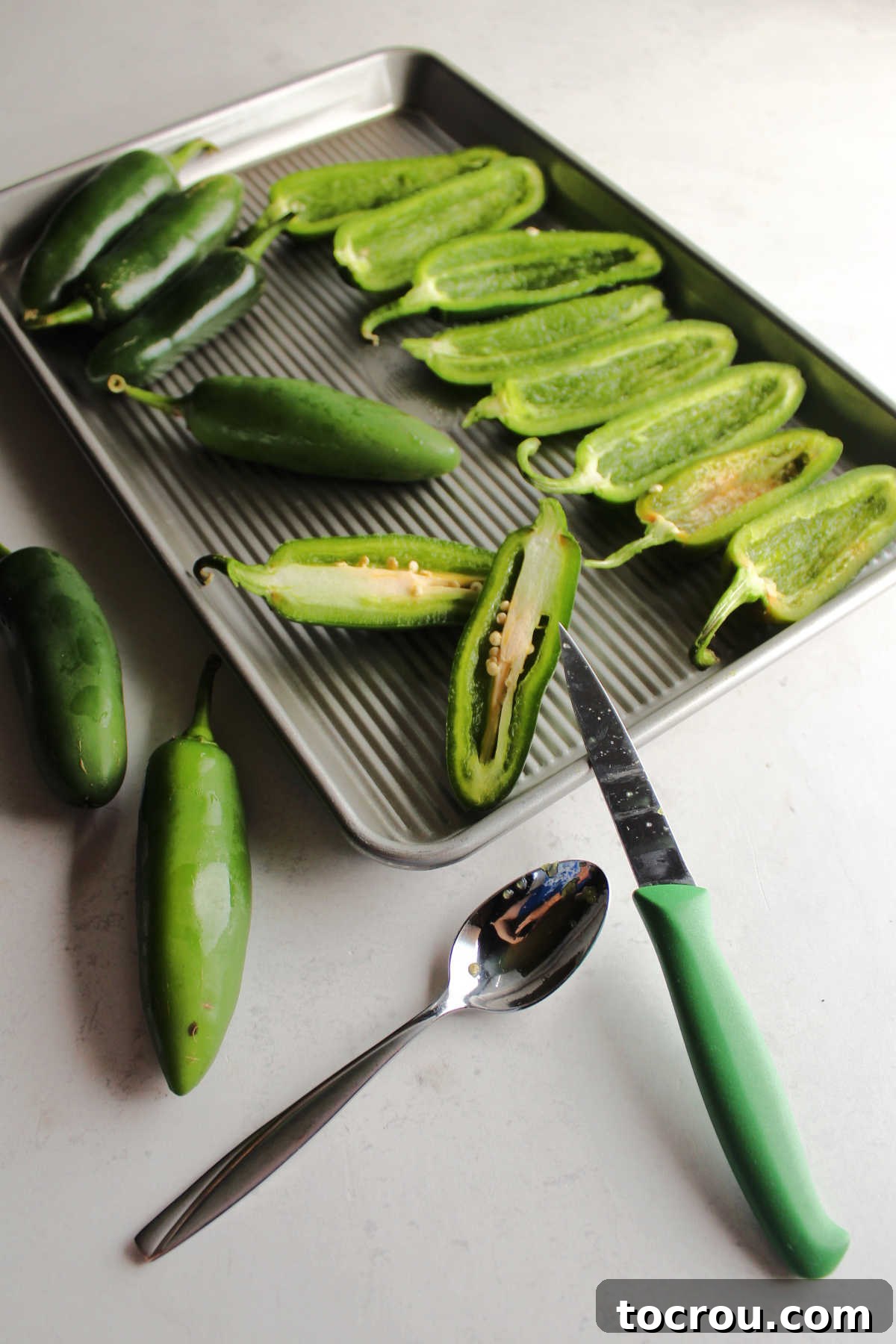 A close-up view of fresh jalapeno peppers being cut in half lengthwise on a cutting board, with seeds and ribs visible, ready for cleaning.