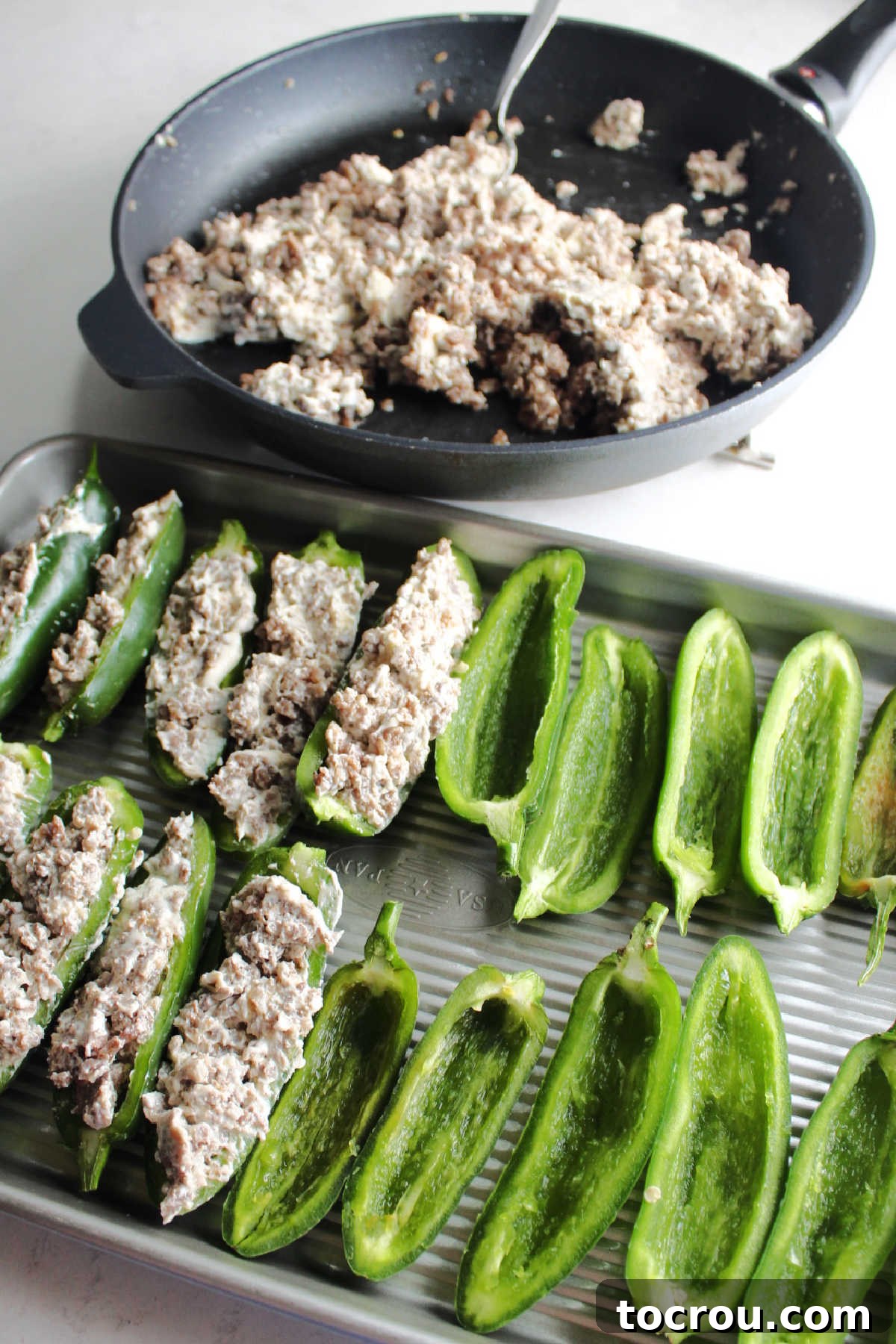 A spoon carefully filling a halved jalapeno pepper with the creamy sausage and cream cheese mixture, ensuring an even and generous amount.