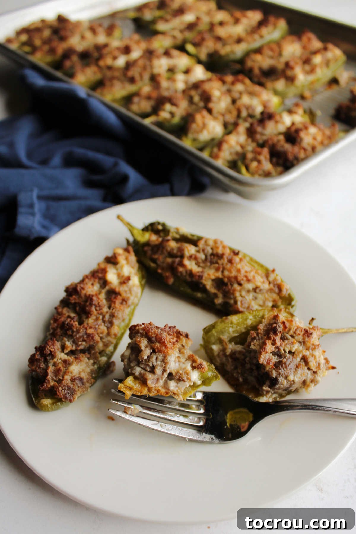A fork holding a single bite of a sausage and cream cheese stuffed jalapeno pepper, showing the delicious golden filling.