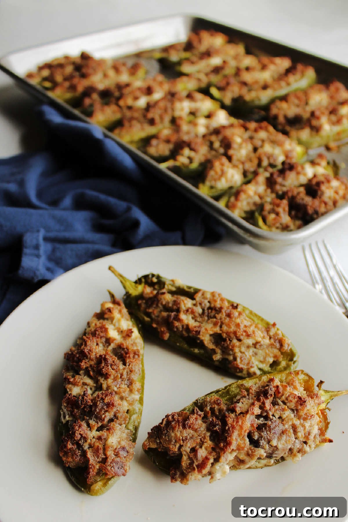 A full plate of creamy sausage stuffed jalapeno poppers in the foreground, with a tray of additional poppers in the background, ready for serving.