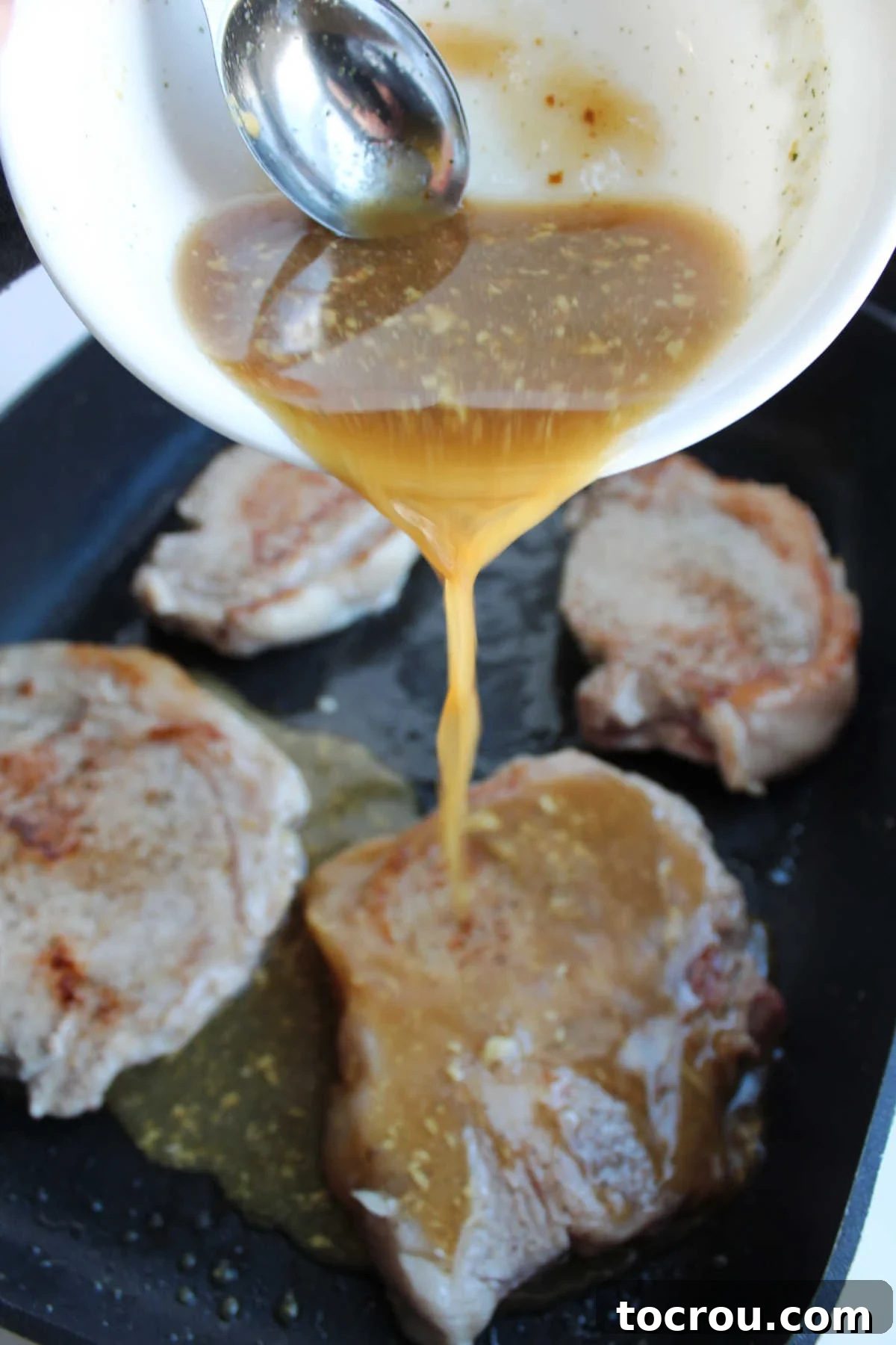 Adding Braising Liquid to Pork Chops Pouring the savory braising liquid over seared pork chops in a large electric skillet, ready for slow simmering.