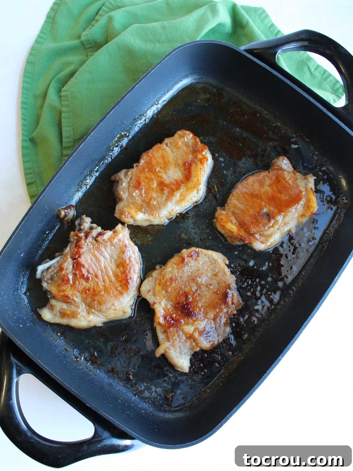 Braised Pork Chops in Skillet with Thickened Sauce Four braised pork chops generously coated with a rich, thickened savory sauce, resting in a large electric skillet.