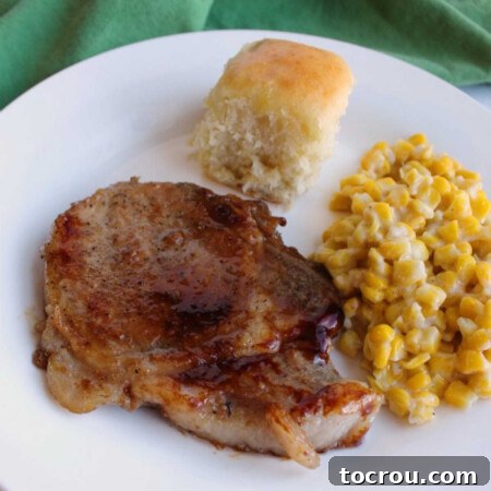 Braised pork chop with thickened sauce served with creamed corn and a homemade Hawaiian roll.