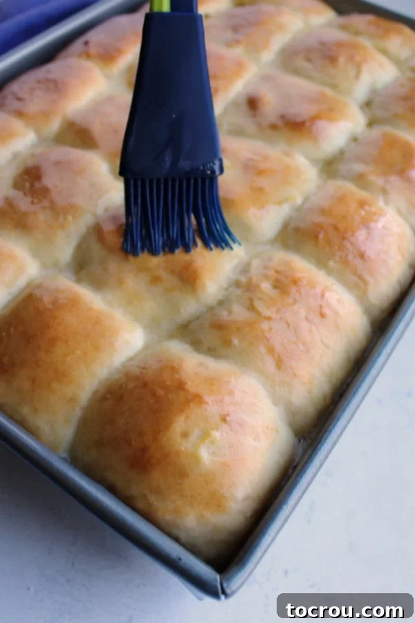 Brushing melted butter over freshly baked golden pineapple rolls.