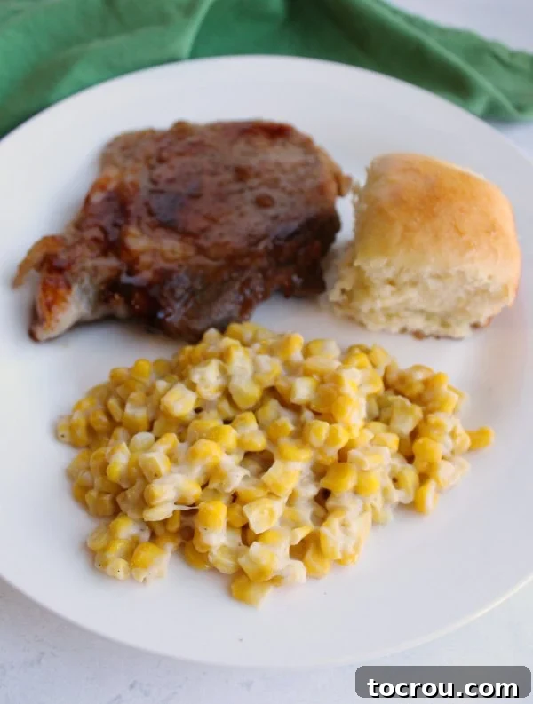 A delicious meal featuring skillet corn, a pork chop, and a homemade Hawaiian roll.