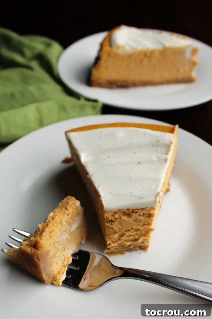 Decadent Pumpkin Cheesecake 3 Bite of pumpkin cheesecake on fork next to slice of creamy pumpkin cheesecake.