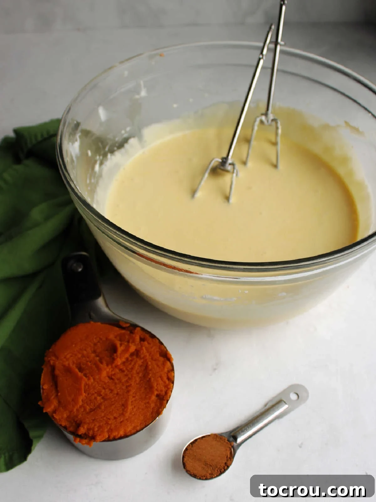 Decadent Pumpkin Cheesecake 5 Bowl of cheesecake mixture next to cup of pumpkin puree and measuring spoon with pumpkin pie spice.