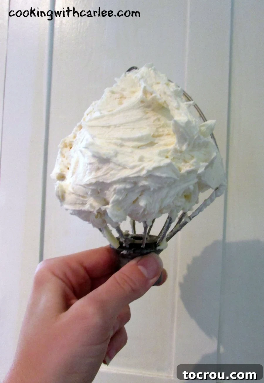 Luscious Condensed Milk Buttercream 3 Mixer whisk loaded with fluffy white condensed milk buttercream.