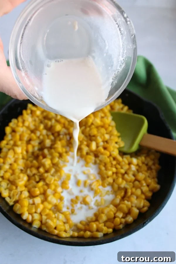 Preparing Creamy Skillet Corn: Adding the Milk Mixture A close-up shot of a hand pouring a creamy milk mixture over vibrant corn kernels in a seasoned cast iron skillet, showcasing the cooking process.