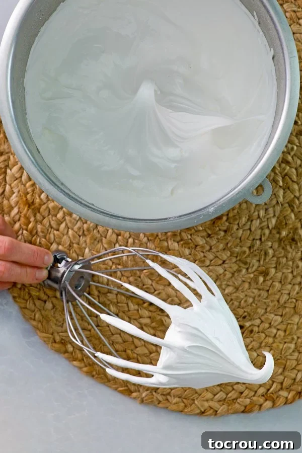 A mixer bowl filled with egg whites, perfectly whipped to stiff, glossy peaks.