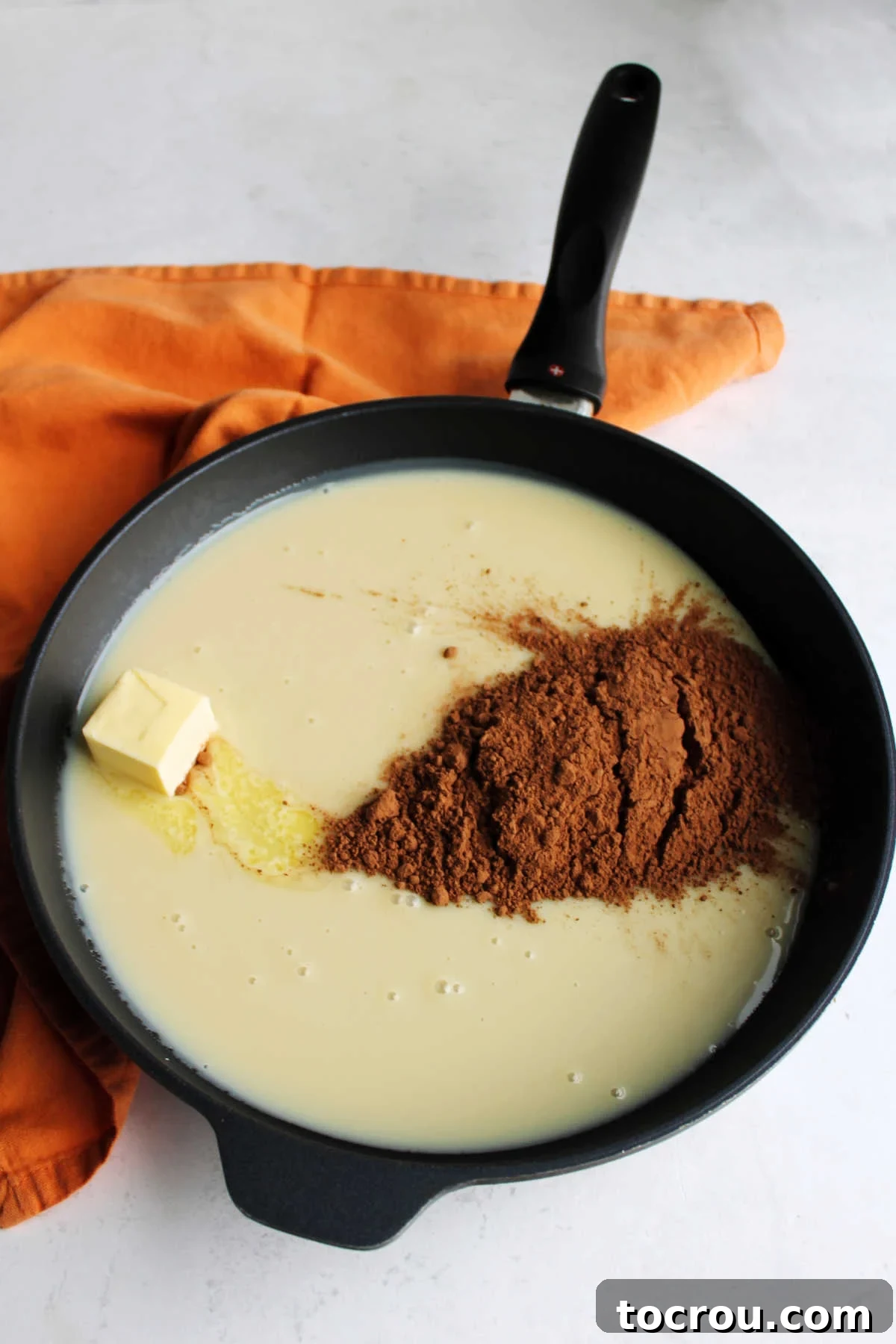 Zesty Chocolate Brigadeiro 4 Sweetened condensed milk, butter, and cocoa powder are combined in a skillet, ready to be cooked into brigadeiro mixture.