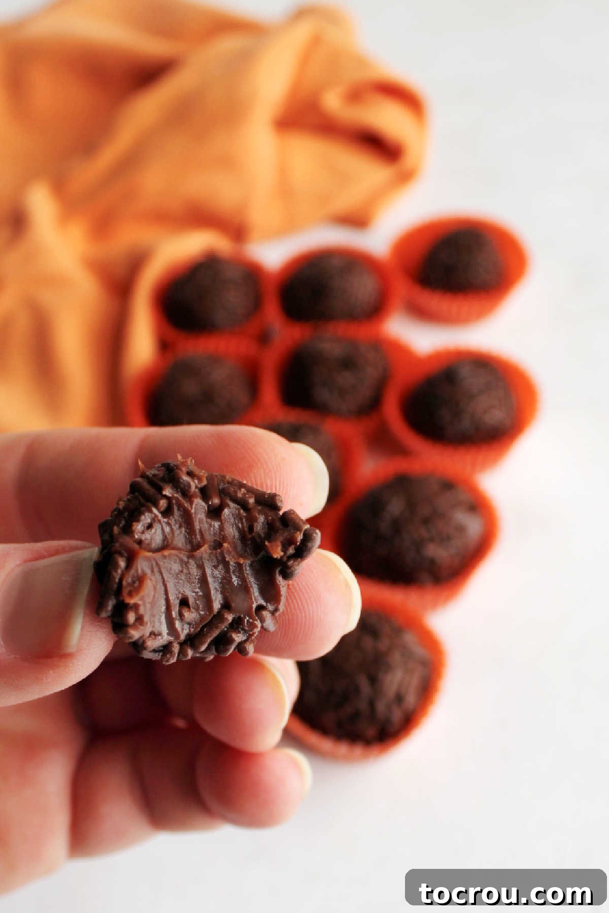Brigadeiros are a delicious chocolate candy from Brazil. They are easy to make and require just a few pantry staples as ingredients. Add a hint of orange to make them an extra special treat! A hand holds a chocolate orange brigadeiro with a bite taken, revealing its soft, luscious interior.
