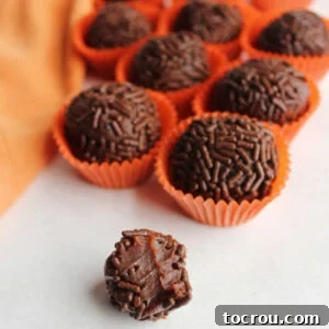 Inside of a chocolate orange brigadeiro with a soft chocolate condensed milk center, surrounded by more sprinkle-coated truffles.