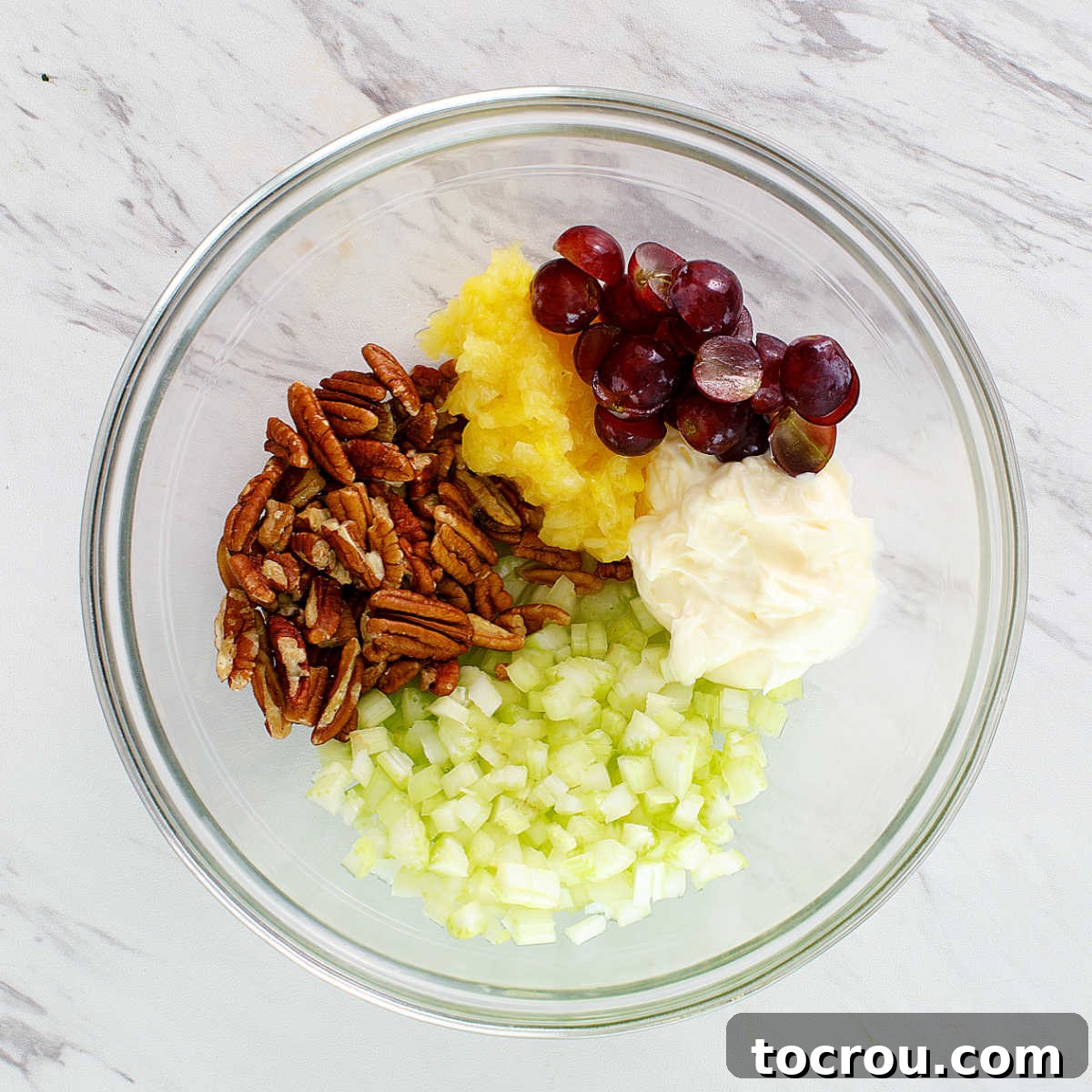 A bowl filled with the fresh, vibrant ingredients for chicken salad, including crunchy nuts, sweet fruit, crisp celery, and the creamy dressing, all ready to be combined.