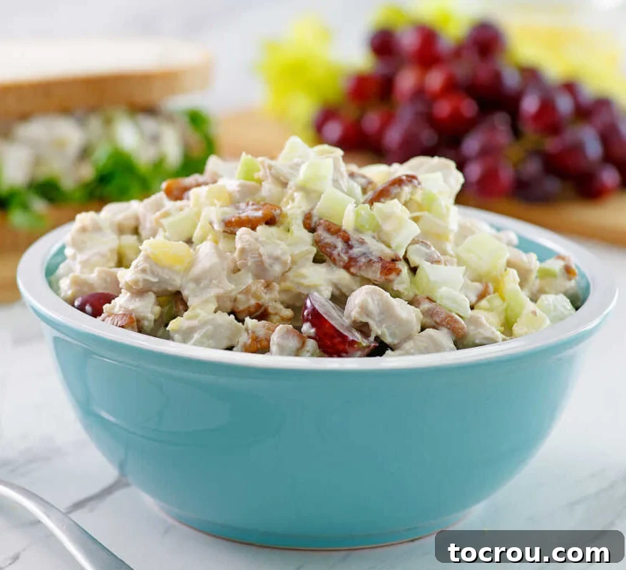 A close-up view of a bowl of chicken salad, perfectly mixed with juicy pineapple chunks and halved grapes, hinting at its readiness to be spread onto a sandwich or served.