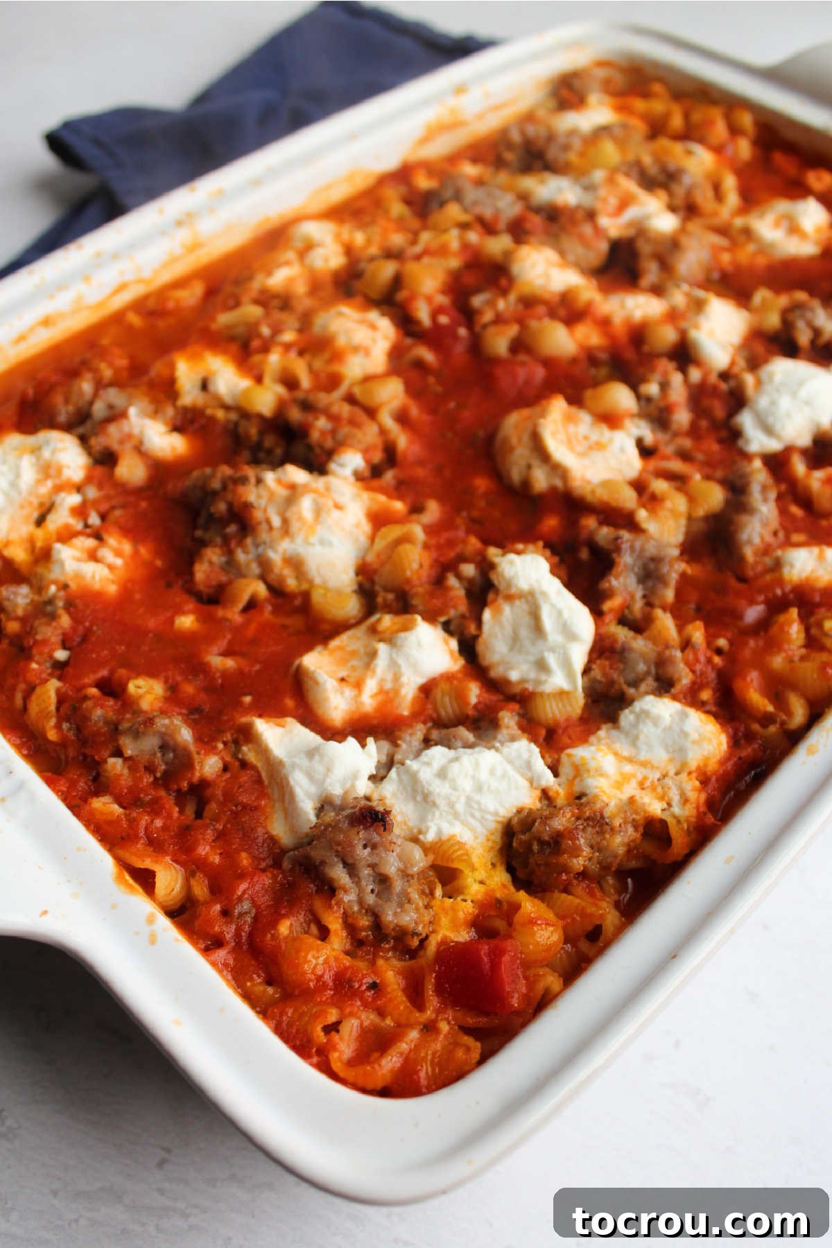 Partially baked no-boil cheesy pasta pan of pasta baked in sauce with sausage and cheese ready for final topping.