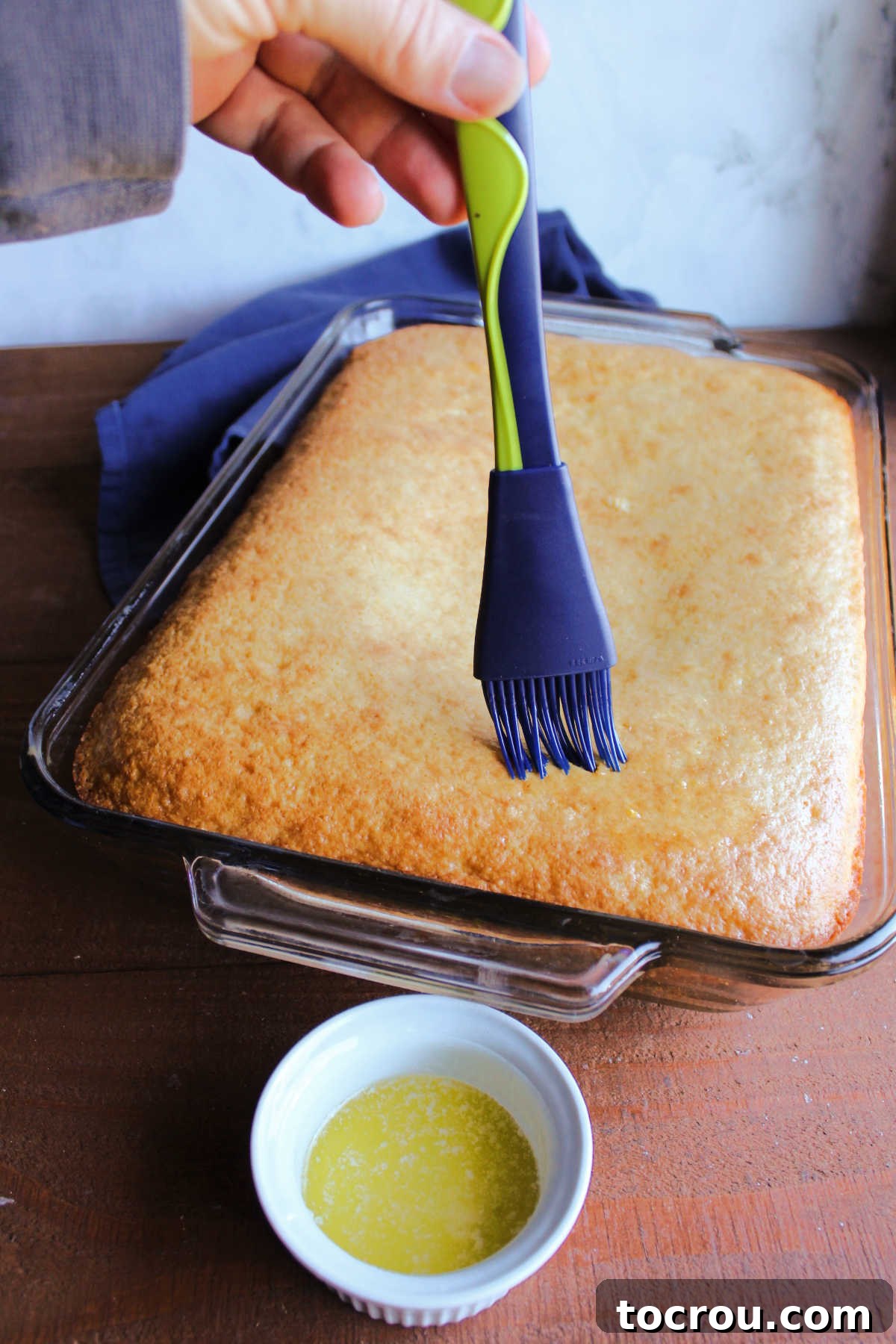 Buttering Warm Cornbread A hand brushing melted butter over the glistening, golden brown top of freshly baked cornbread.