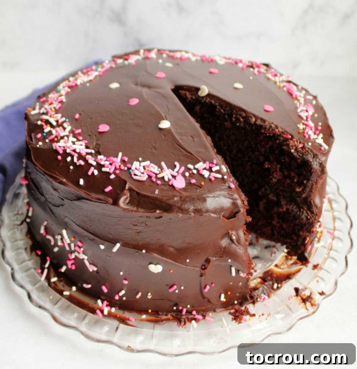 Rich Chocolate Comfort Cake with Velvety Frosting 2 A beautifully layered chocolate cake, expertly frosted with shiny chocolate icing and adorned with vibrant sprinkles, ready to be enjoyed.