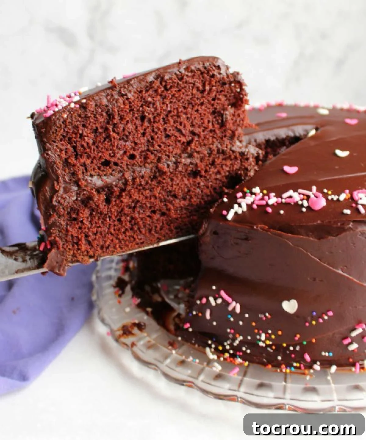 Rich Chocolate Comfort Cake with Velvety Frosting 7 A delectable slice of layered chocolate wacky cake is lifted from the cake, revealing rich layers of fudge frosting both between the cake layers and on its exterior.