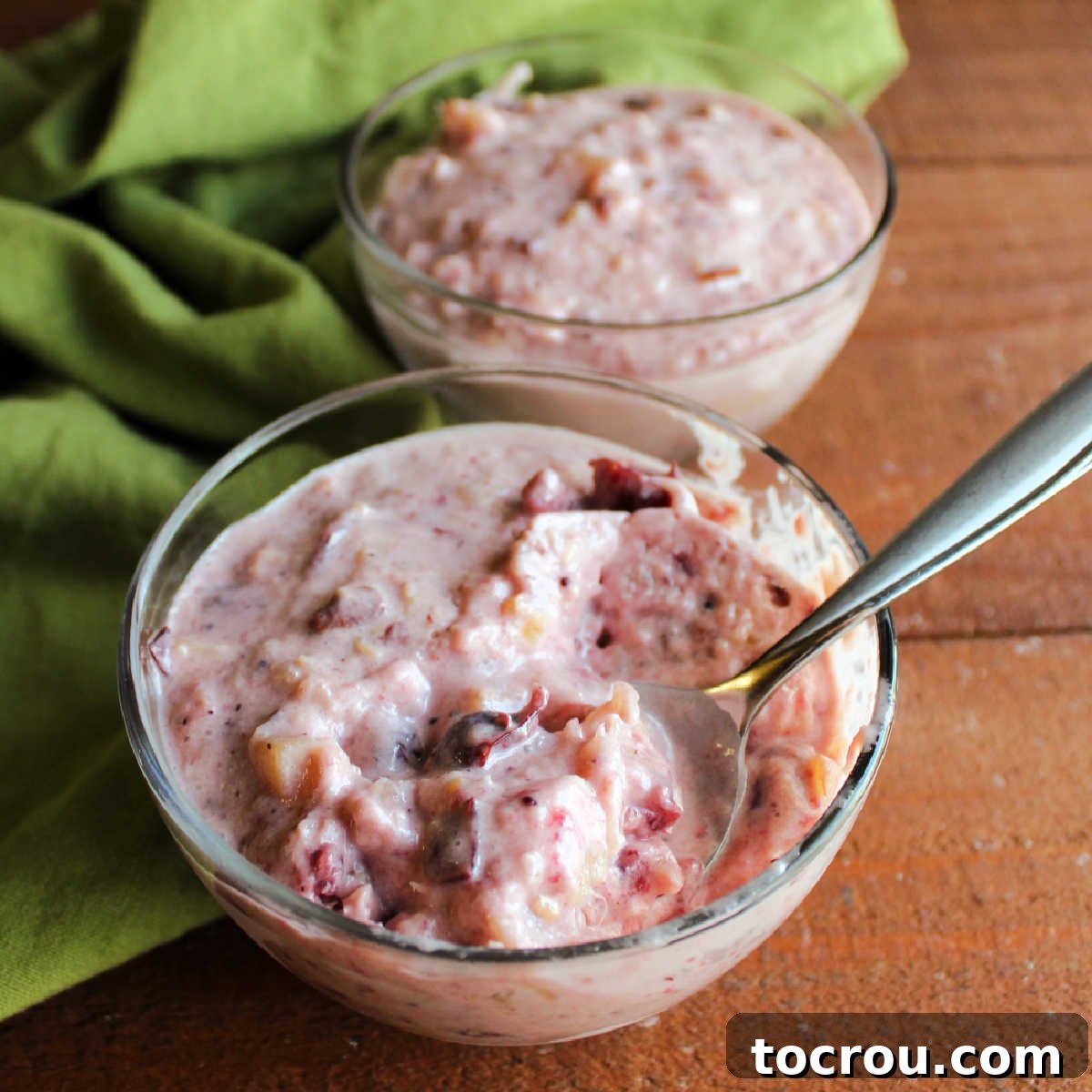 Spoon in small glass bowl filled with creamy frozen cranberry pineapple salad, highlighting its smooth texture and vibrant color.