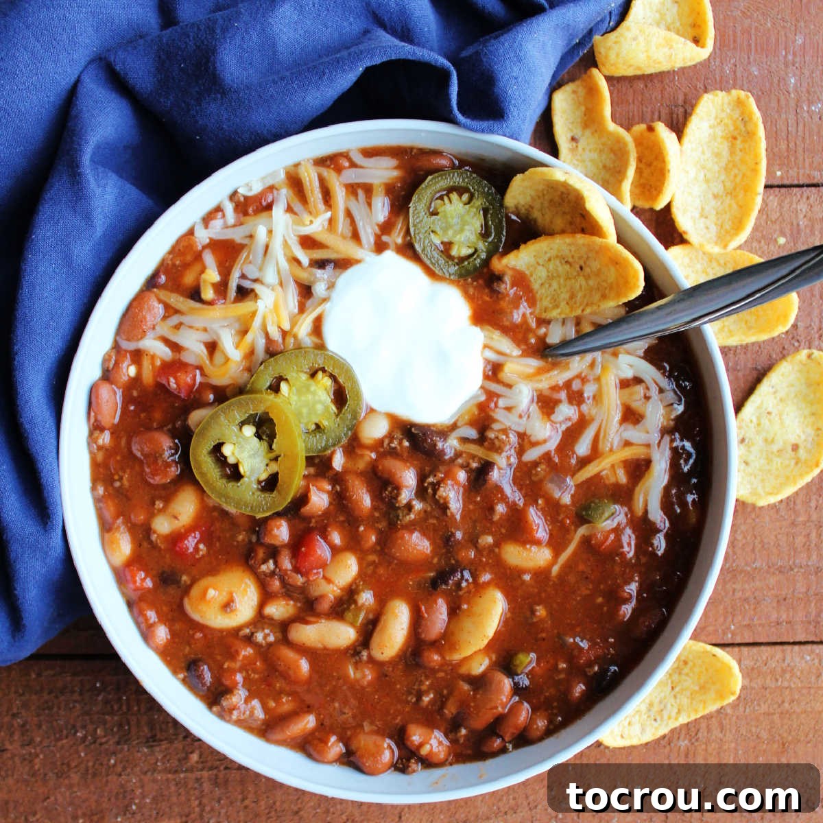 Bowl of venison chili with lots of beans topped with shredded cheese, jalapenos and a dollop of sour cream. 