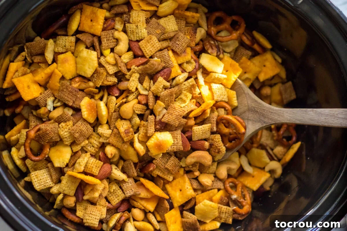 Crockpot filled with Chex Mix with crackers, nuts, and cereal in spice mix. 