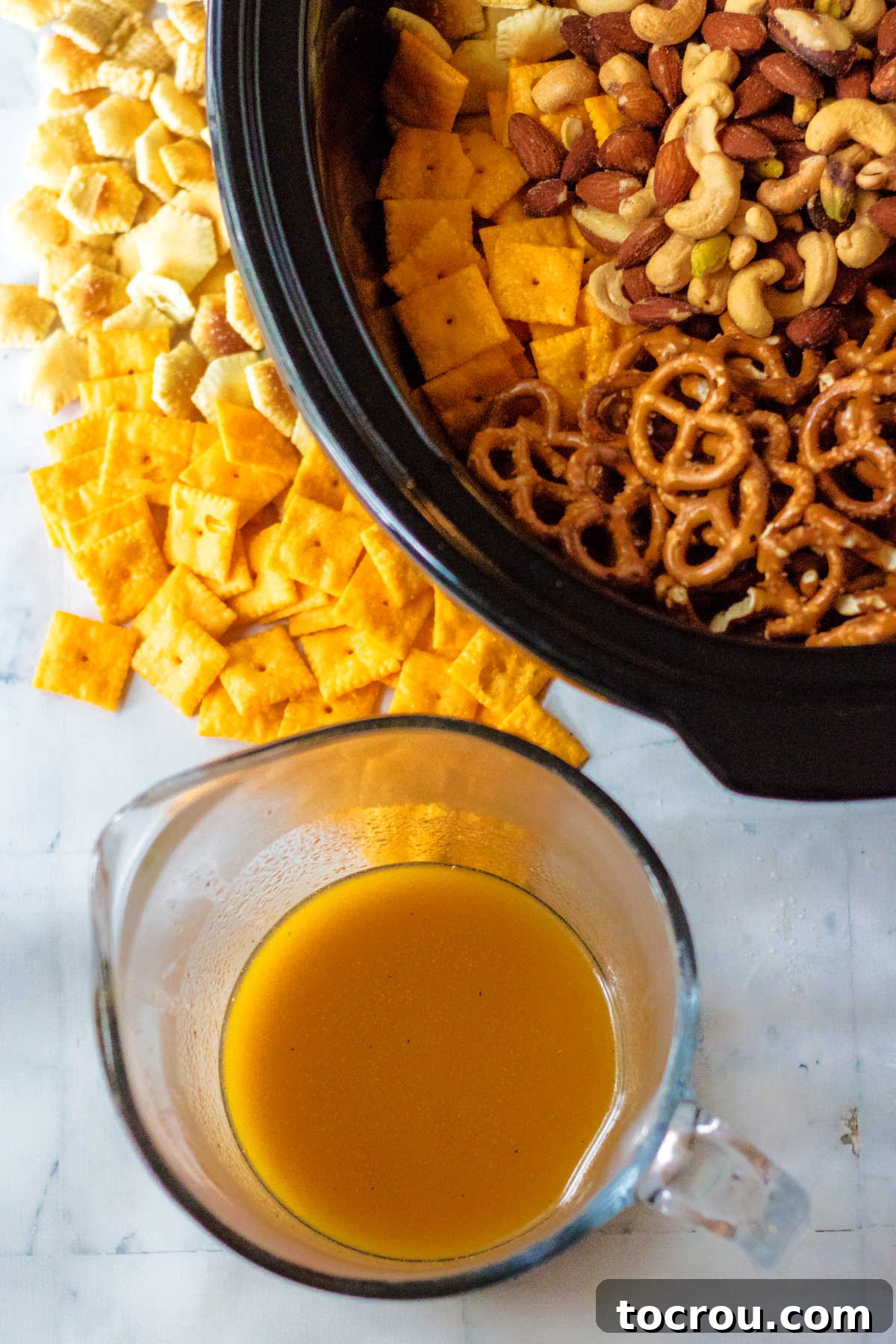 Measuring cup with butter spice mix next to crock pot filled with cereal and crackers etc.