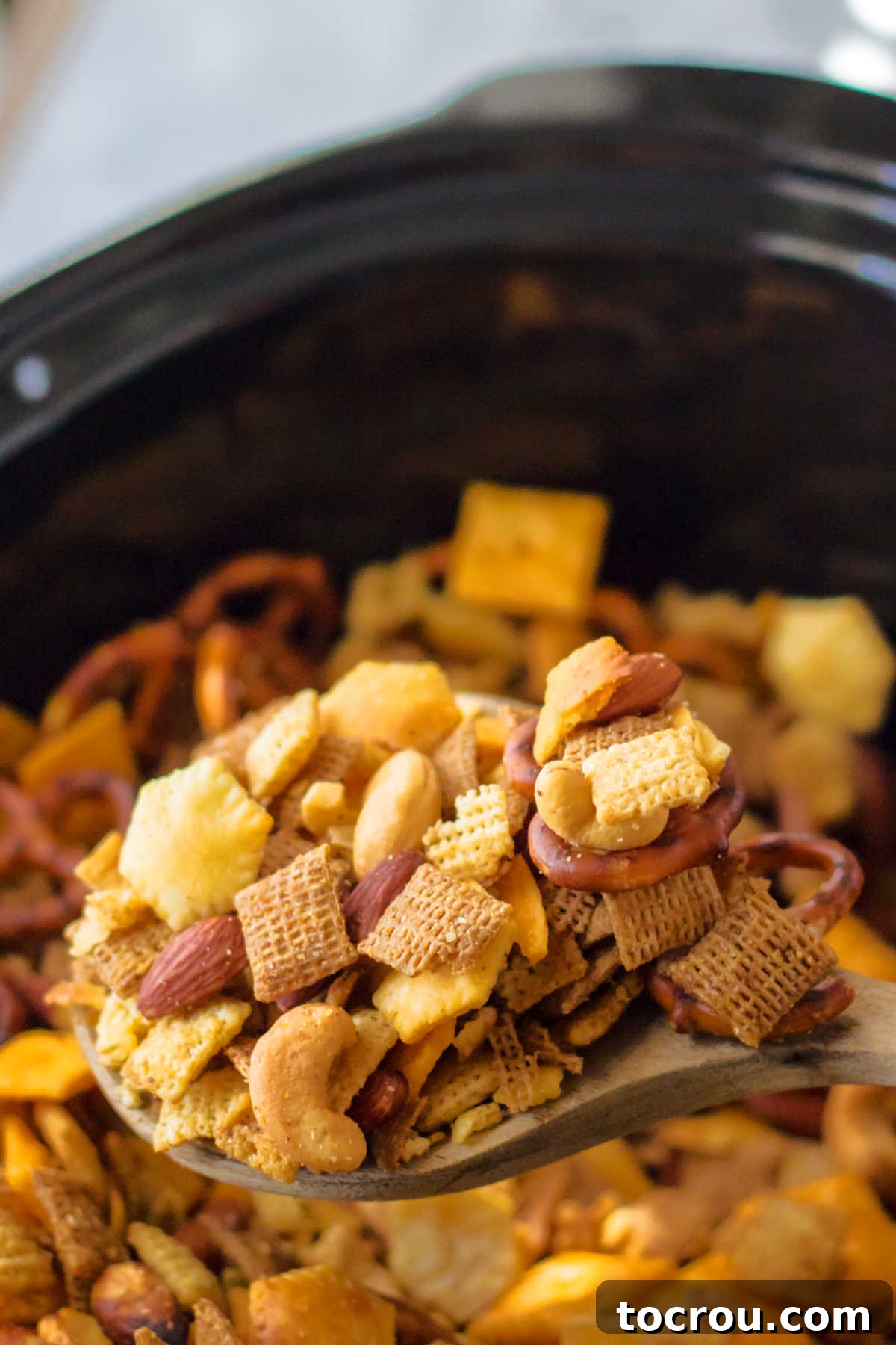 Spoon lifting scoop of finished chex mix out of slow cooker.