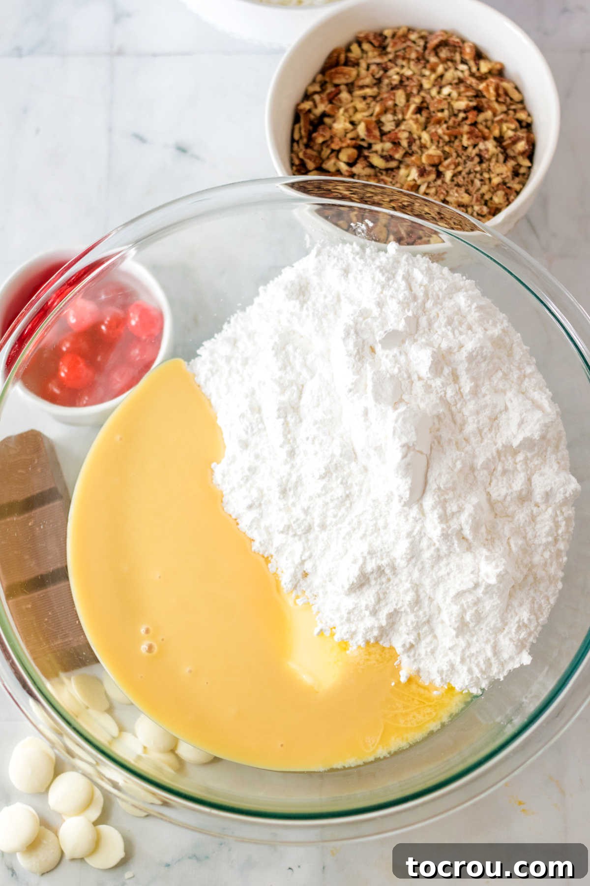 Glass mixing bowl containing powdered sugar, sweetened condensed milk, and softened butter, ready to be combined for the candy filling.