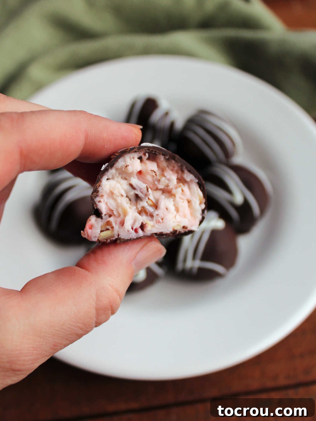 A hand holding half of a Martha Washington candy, clearly showing the creamy interior filled with bits of pecans, shredded coconut, and vibrant maraschino cherries.