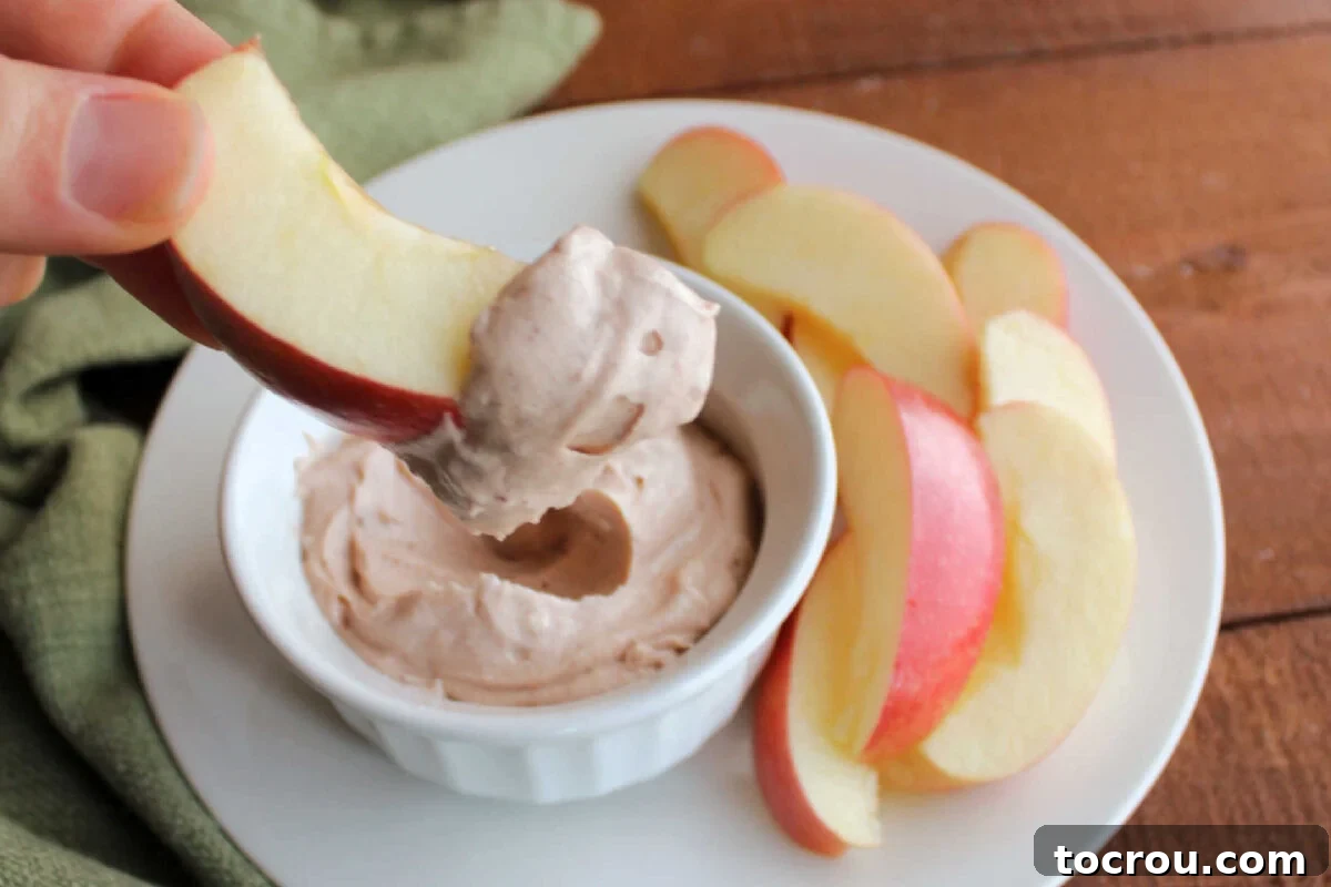 Hand holding an apple slice generously coated with smooth and creamy apple butter dip, ready to be enjoyed.