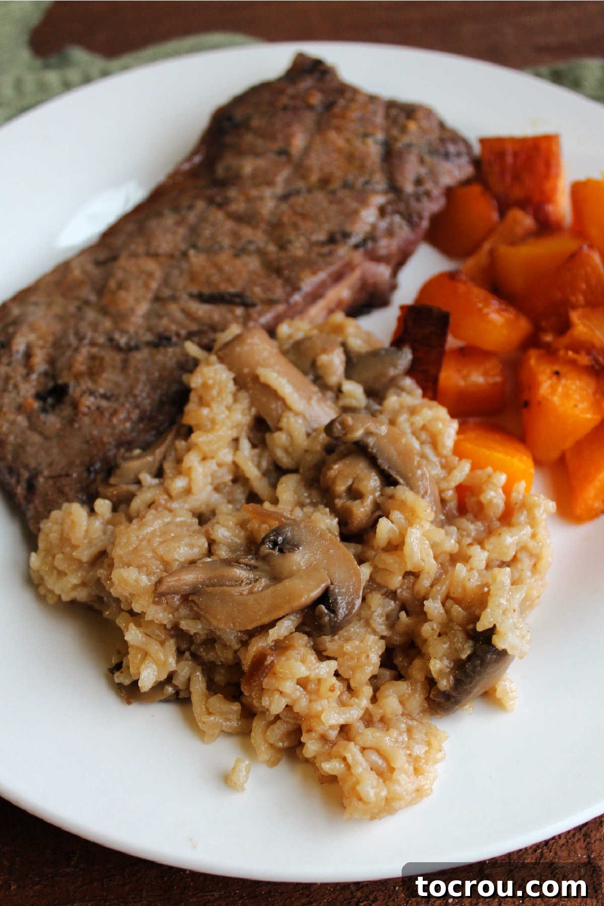 Homestyle Mushroom Rice Bake 5 Mushroom baked rice served on dinner plate with steak and roasted butternut squash.