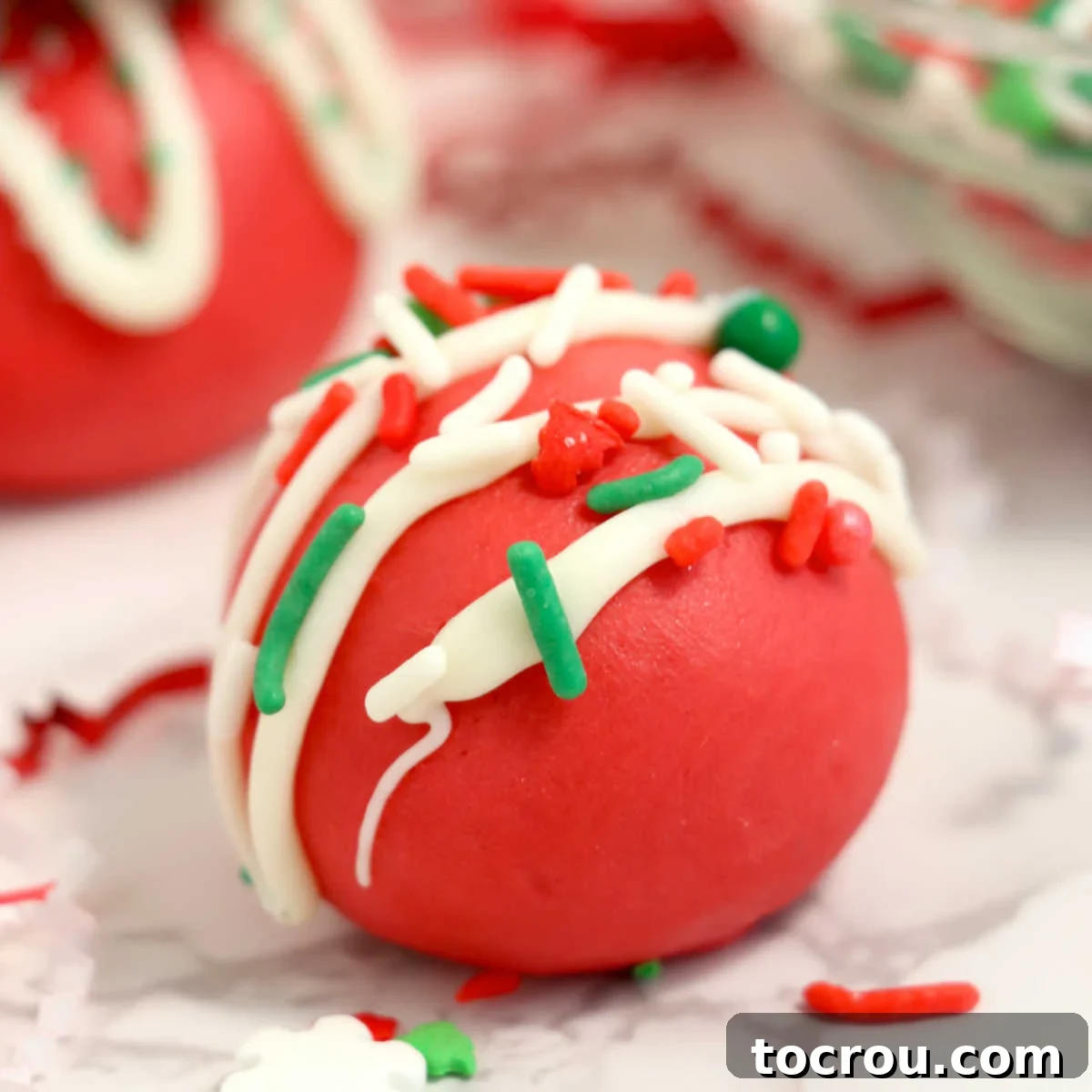 Close up of smooth red velvet truffles topped with white chocolate drizzle and Christmas sprinkles, showcasing their vibrant color and festive appeal.