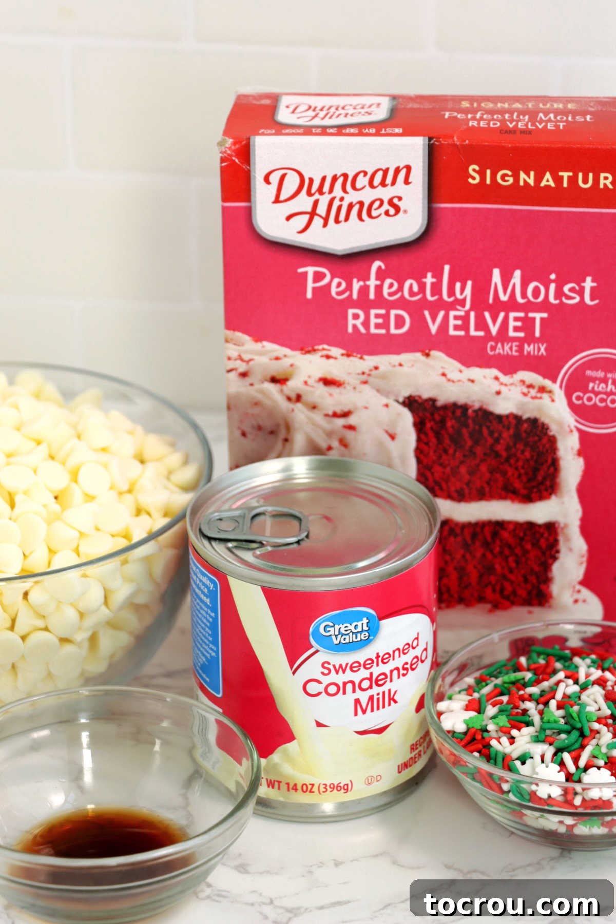 Ingredients: white chocolate chips, vanilla extract, sweetened condensed milk and red velvet cake mix, laid out ready to be transformed into truffles.