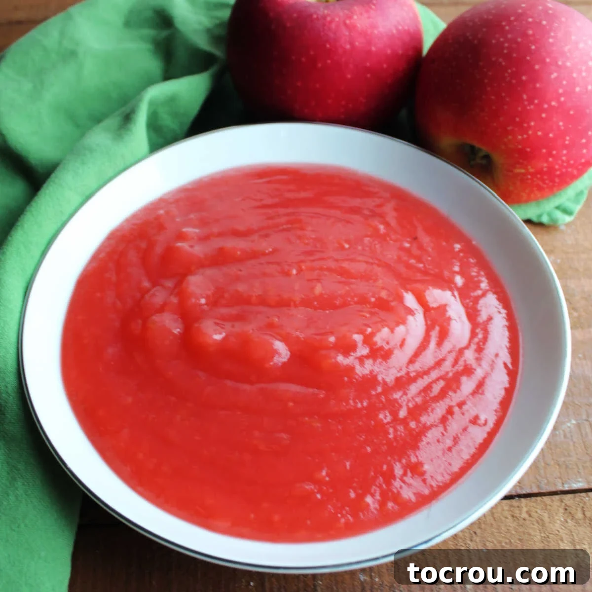 A bowl of smooth, rosy red applesauce, flavored with cinnamon candies, ready to be enjoyed.