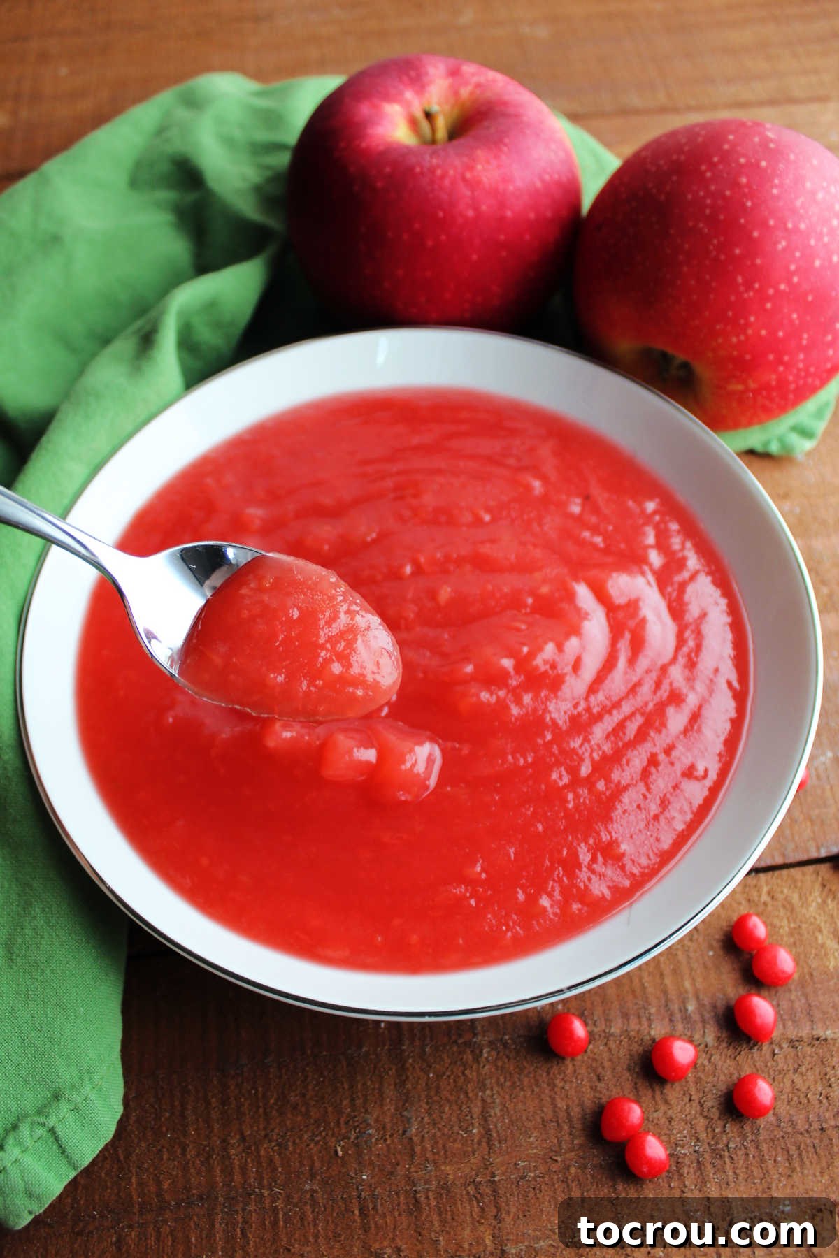 A spoon with a bite of luscious red cinnamon applesauce, perfectly ready to be tasted and enjoyed.