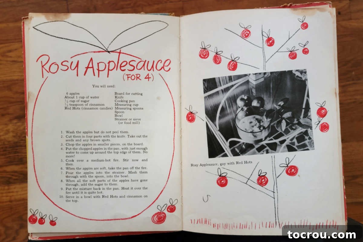 An open vintage cookbook with yellowed pages and charming illustrations, showing a recipe for rosy applesauce.