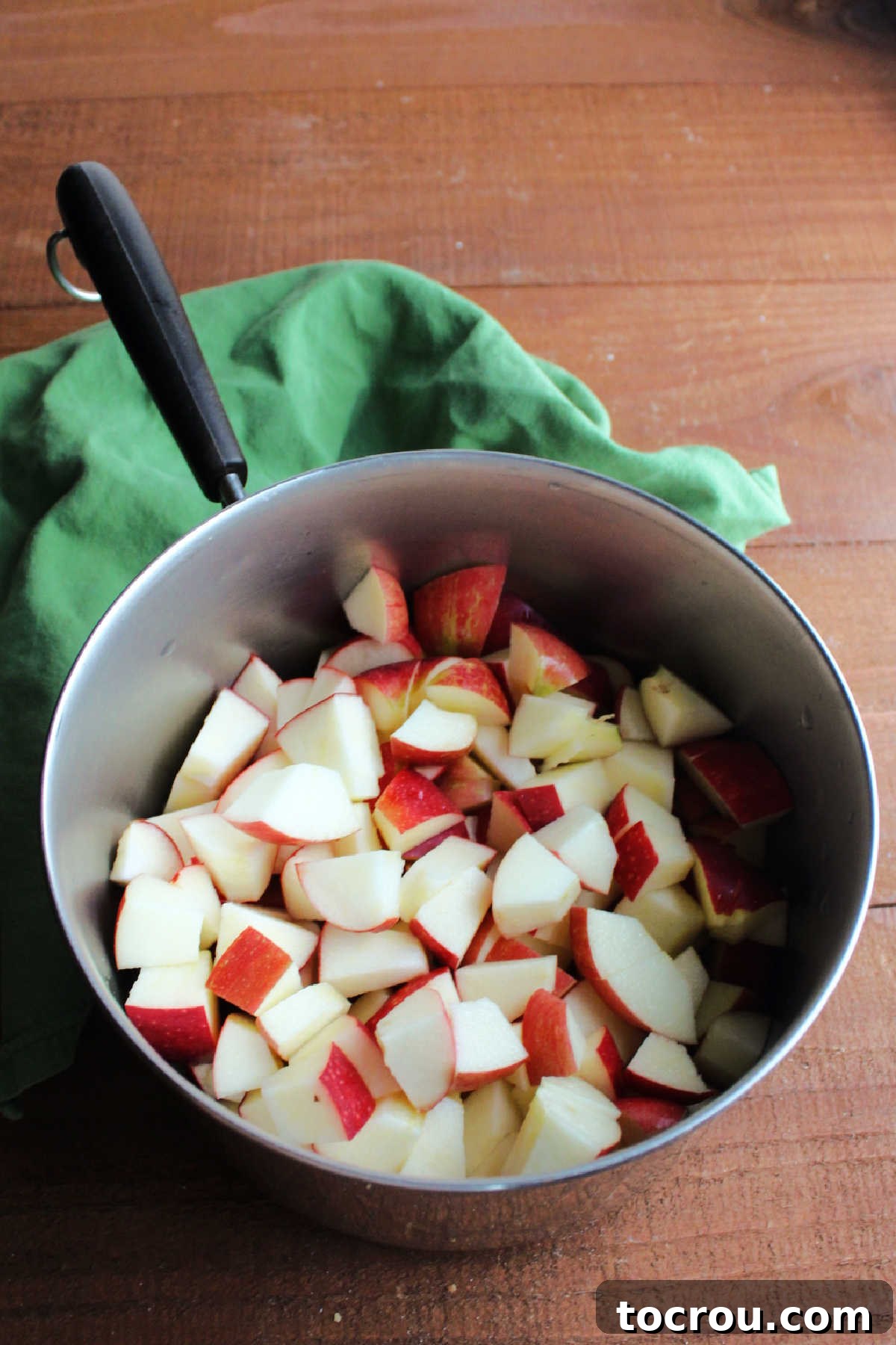 Chunks of unpeeled apples in a saucepan with water, prepared for cooking to make homemade applesauce.