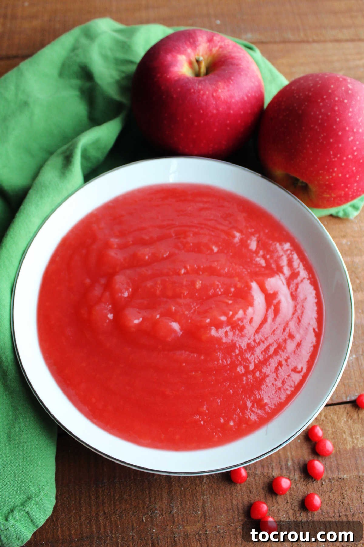 A charming bowl of homemade red hot applesauce, garnished with fresh apple slices and a scattering of red hot candies for decoration.