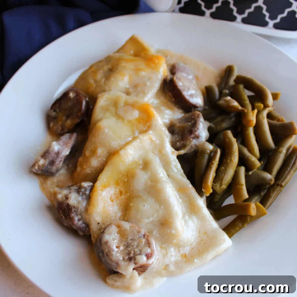 Close up of cheesy pirogies and chunks of kielbasa in a sour cream sauce served with green beans. 