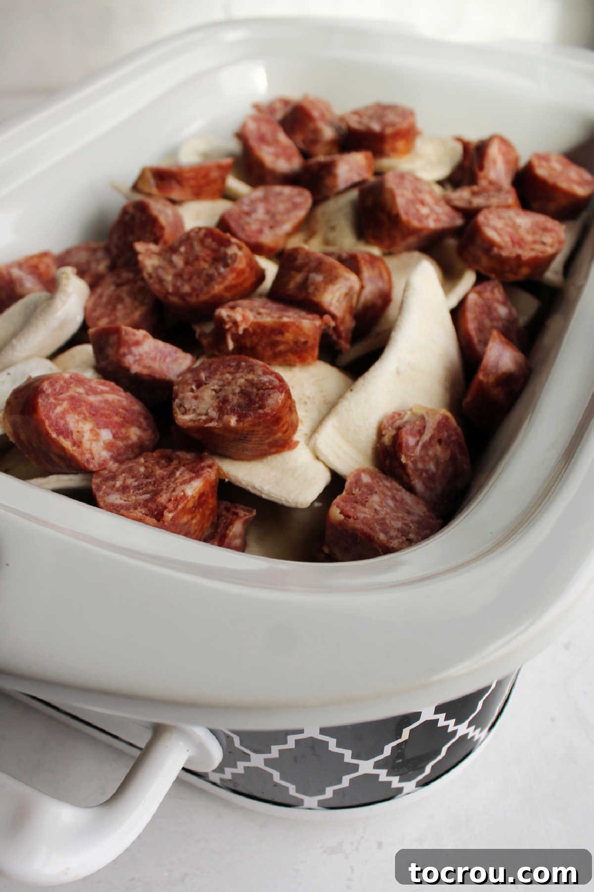 Frozen pierogies, chicken broth and sliced keilbasa in crockpot ready to cook.