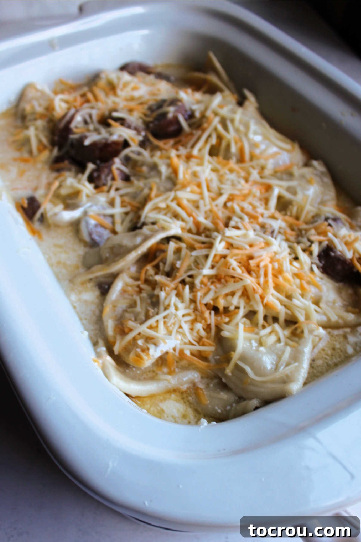 Cooked sausage and pierogies with sour cream and cheese mixed in and extra shredded cheese on top ready to finish cooking.