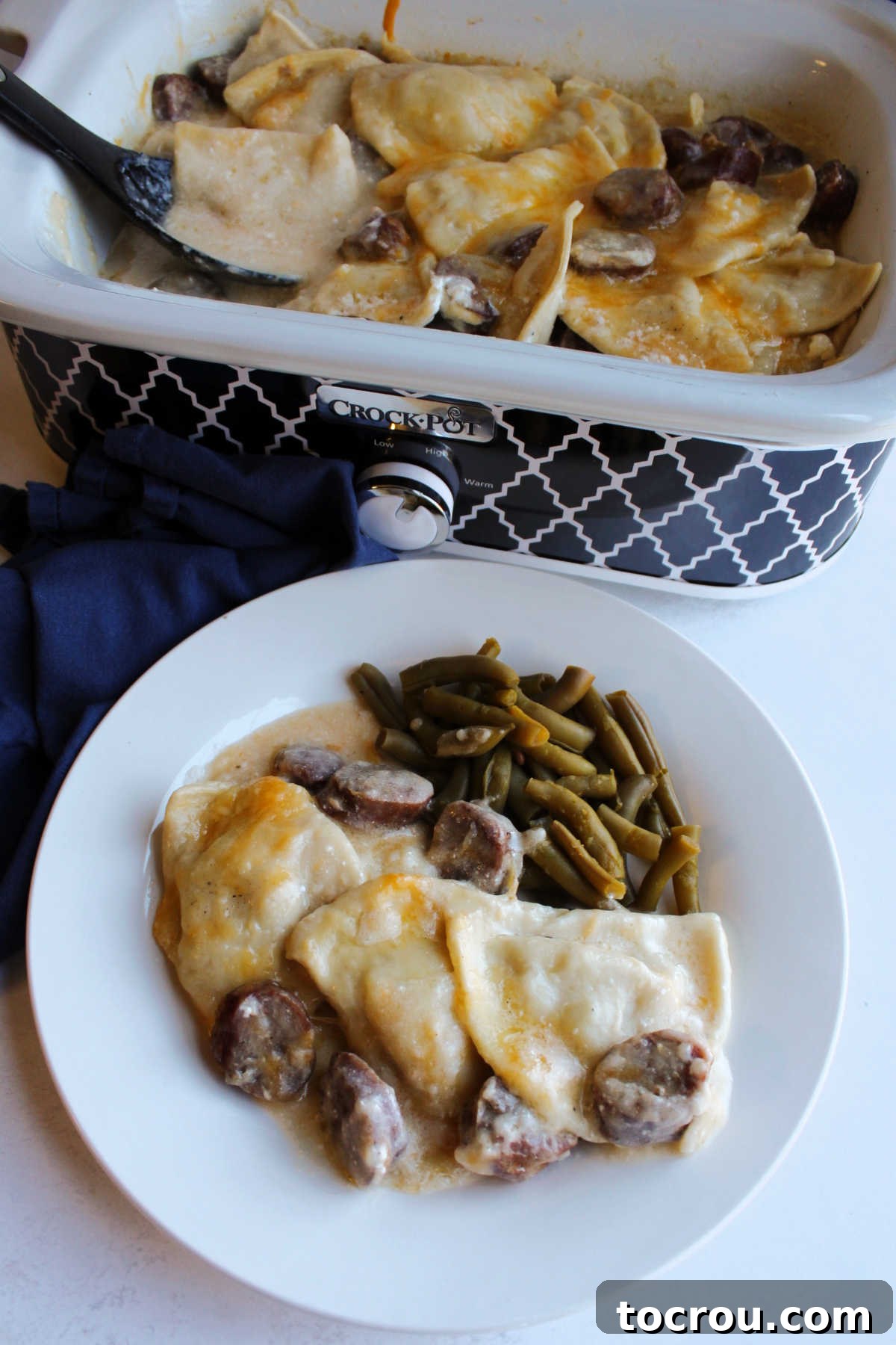 Plate of creamy pierogis and smoked sausage casserole with green beans by slow cooker with remaining pierogi. 