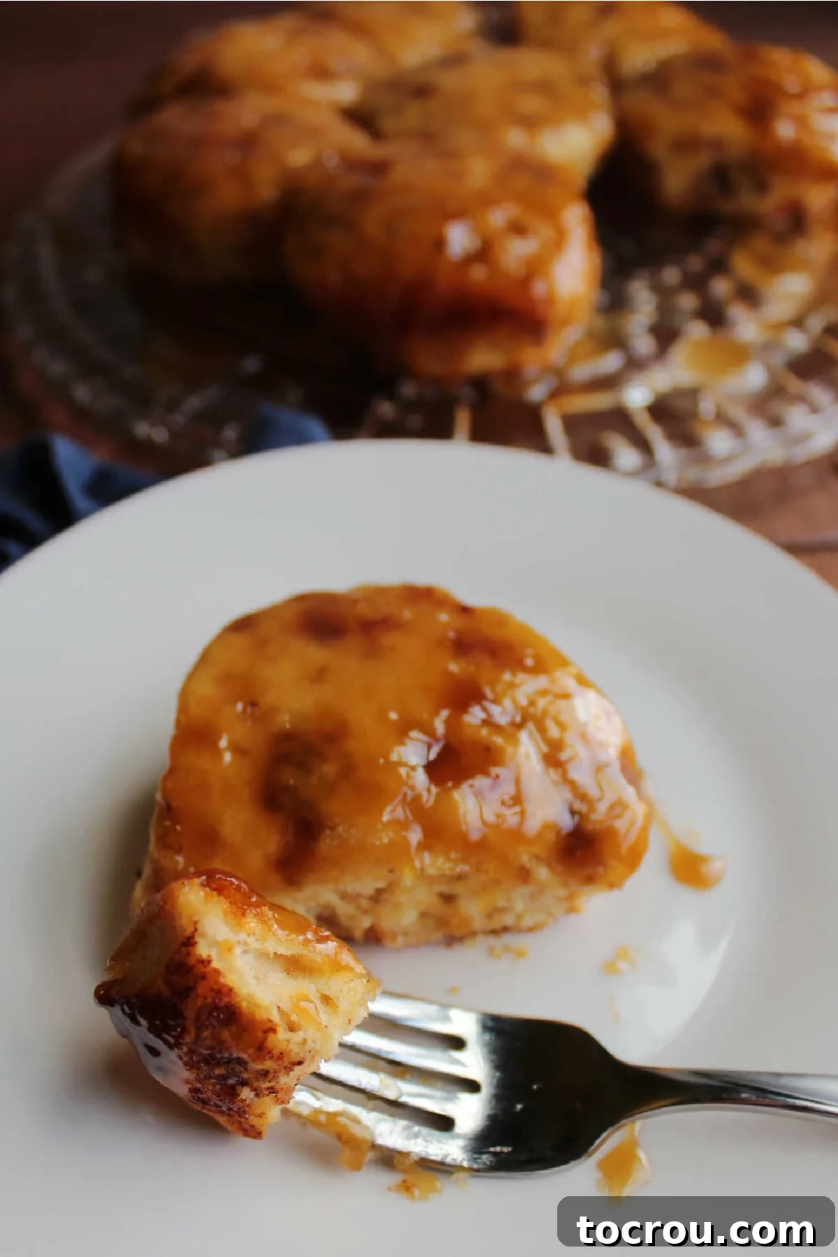 A delectable bite of a soft and gooey maple cinnamon bun held aloft on a fork, the rich caramel sauce dripping slightly, poised for eating.