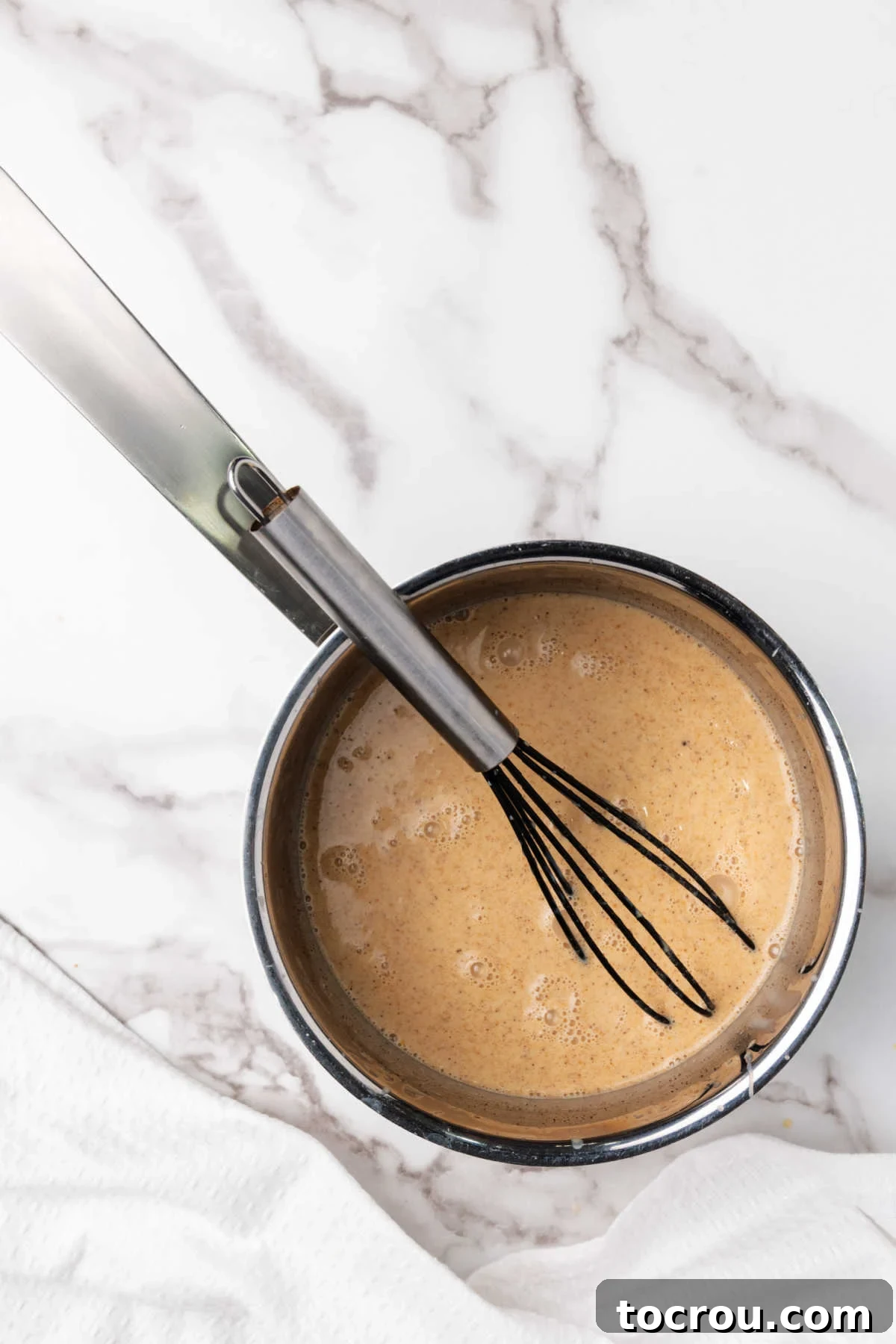 Saucepan filled with pumpkin spice coffee creamer, with a whisk resting inside, showing the creamy texture and readiness for serving.