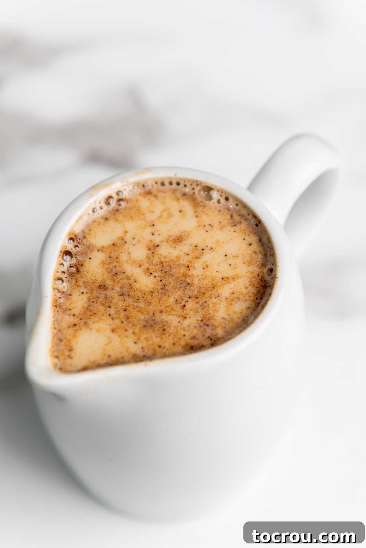 Small white pitcher filled with freshly made homemade pumpkin spice creamer, ready to be poured, showcasing its rich, smooth texture.